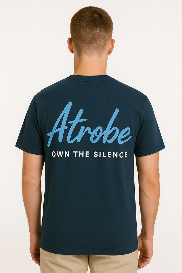 Jonge man in een donkerblauw T-shirt met de lichtblauwe tekst "Atrobe" zn rug met eronder own the silence, staand voor een neutrale witte achtergrond.